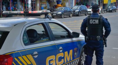 Agente da Guarda Civil de Aparecida patrulha região comercial ao lado de viatura, reforçando a segurança e presença preventiva nas ruas da cidade.