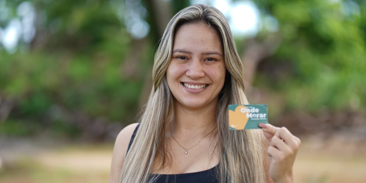 Foto de uma mulher segurando o cartão do benefício do Alguel social.