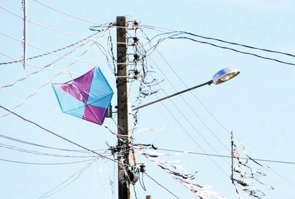 Imagem mostra uma pipa azul e roxa presa em fios de alta tensão, evidenciando o risco de acidentes com a rede elétrica em áreas urbanas.