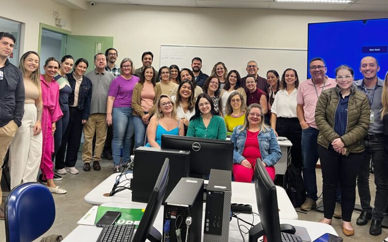 A imagem mostra um grupo de profissionais reunidos em sala de treinamento, posando para foto coletiva.