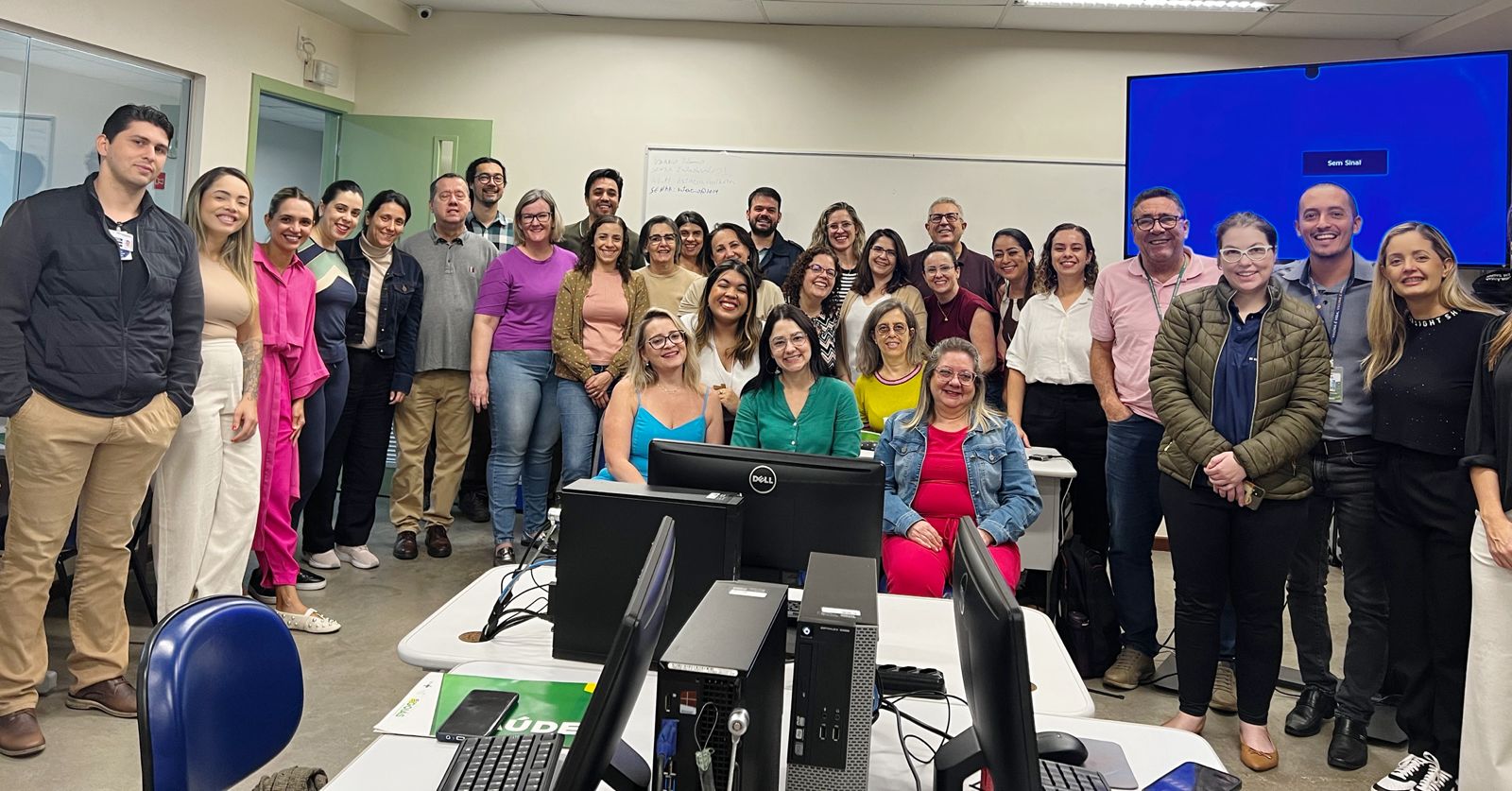 A imagem mostra um grupo de profissionais reunidos em sala de treinamento, posando para foto coletiva.